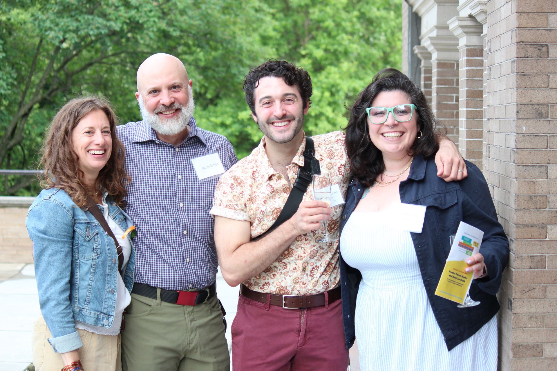 Four people smiling outdoors, standing arm in arm near a brick building.