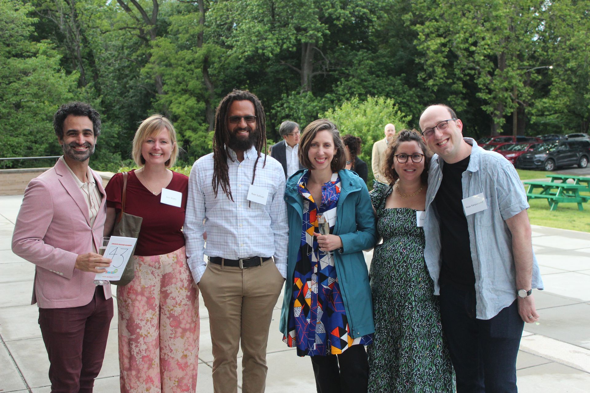 Six people posing outdoors, smiling in casual and dressy clothes in a park-like setting.