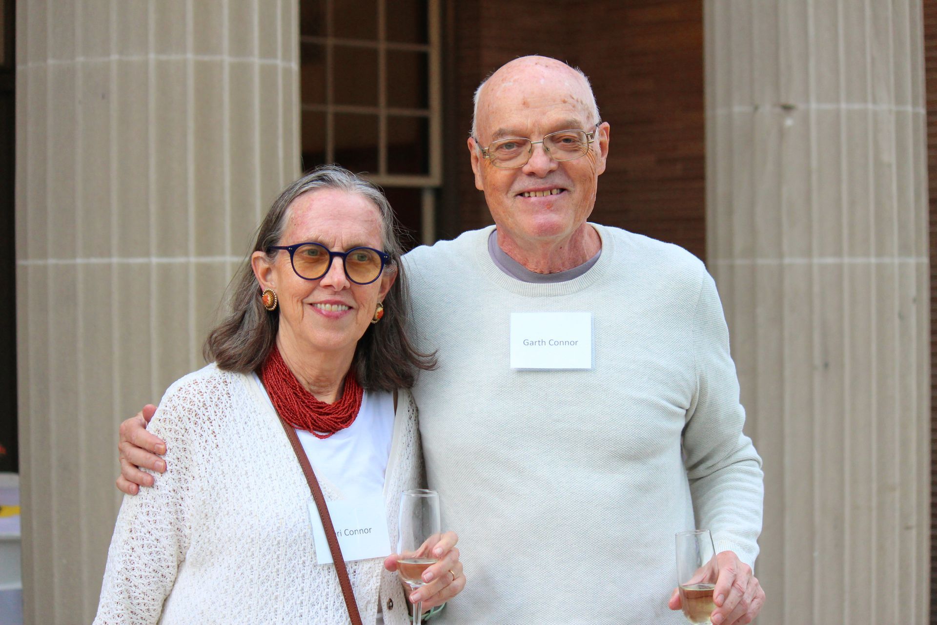 Two smiling people stand together outside a building with tall columns.