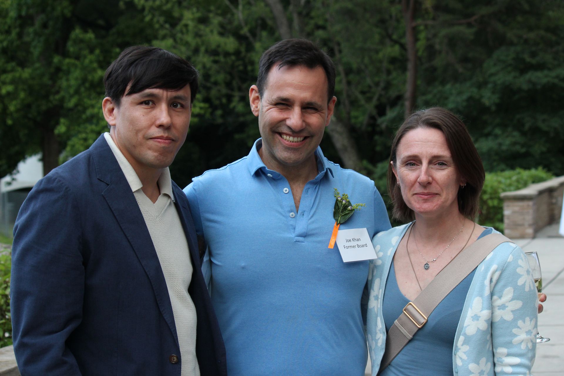 Three people standing outdoors, smiling at the camera, wearing casual jackets and a blue shirt.
