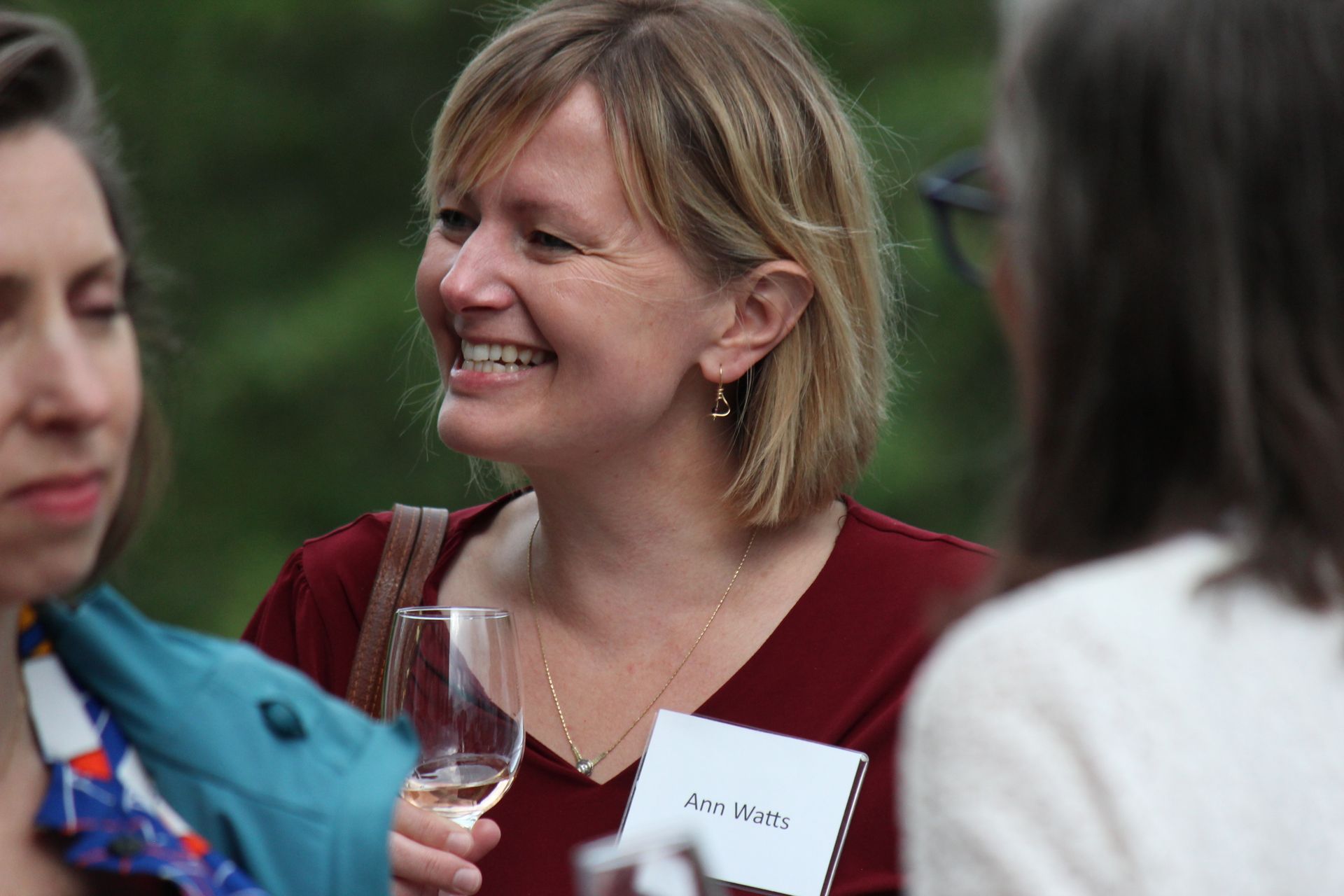 Smiling woman in a red top holding a wine glass at an outdoor gathering