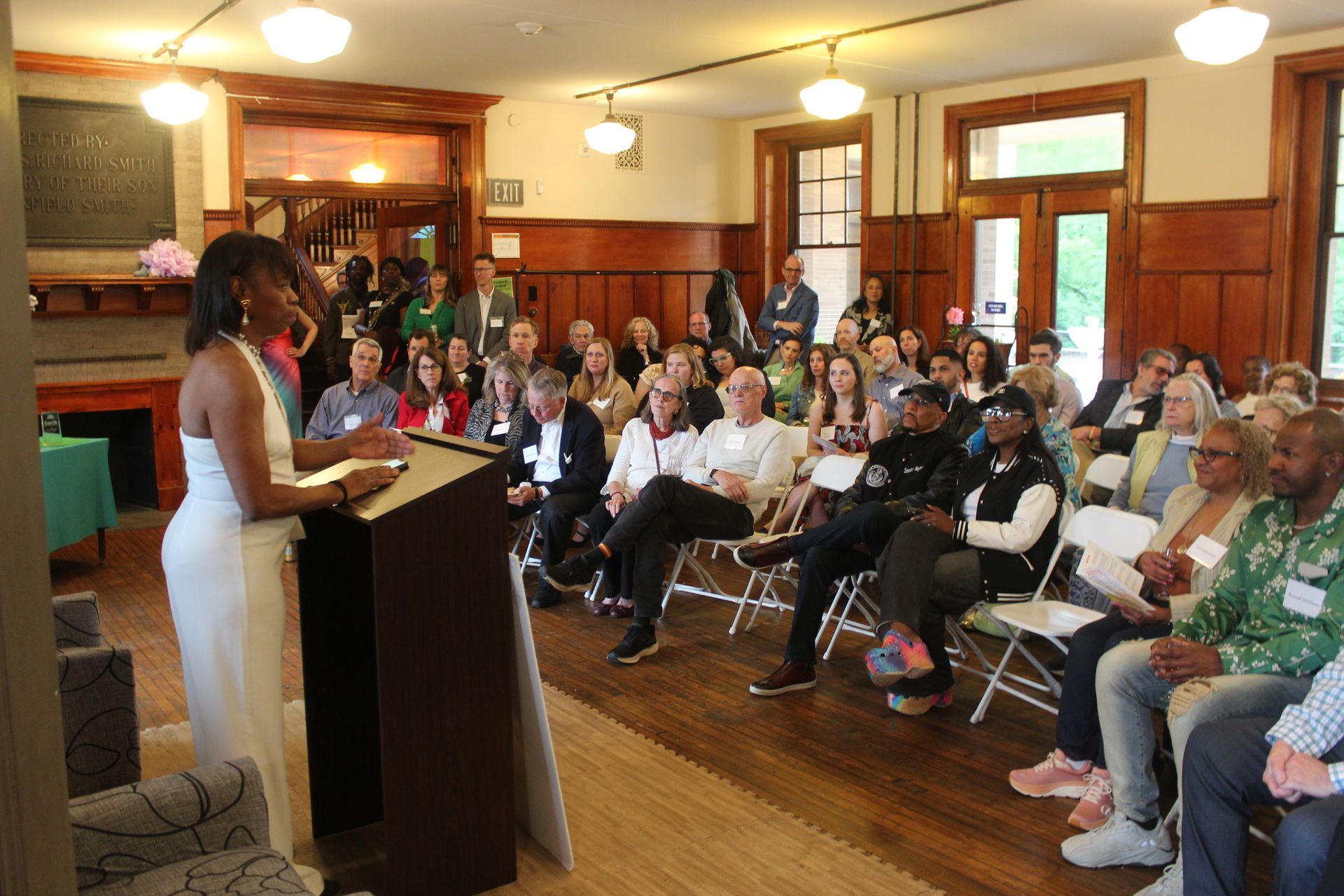 Woman speaking at a podium to an audience seated in a wood-paneled room