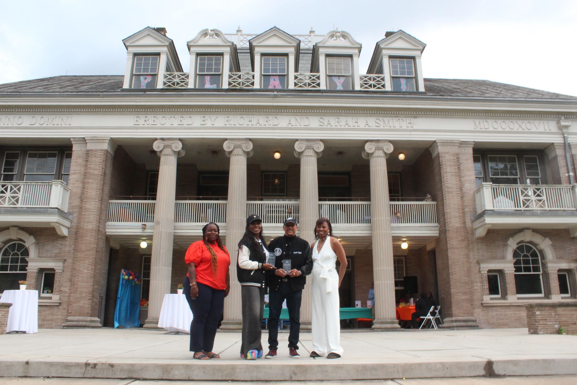 Five people pose on the steps of a large mansion-style building with columns and dormer windows.