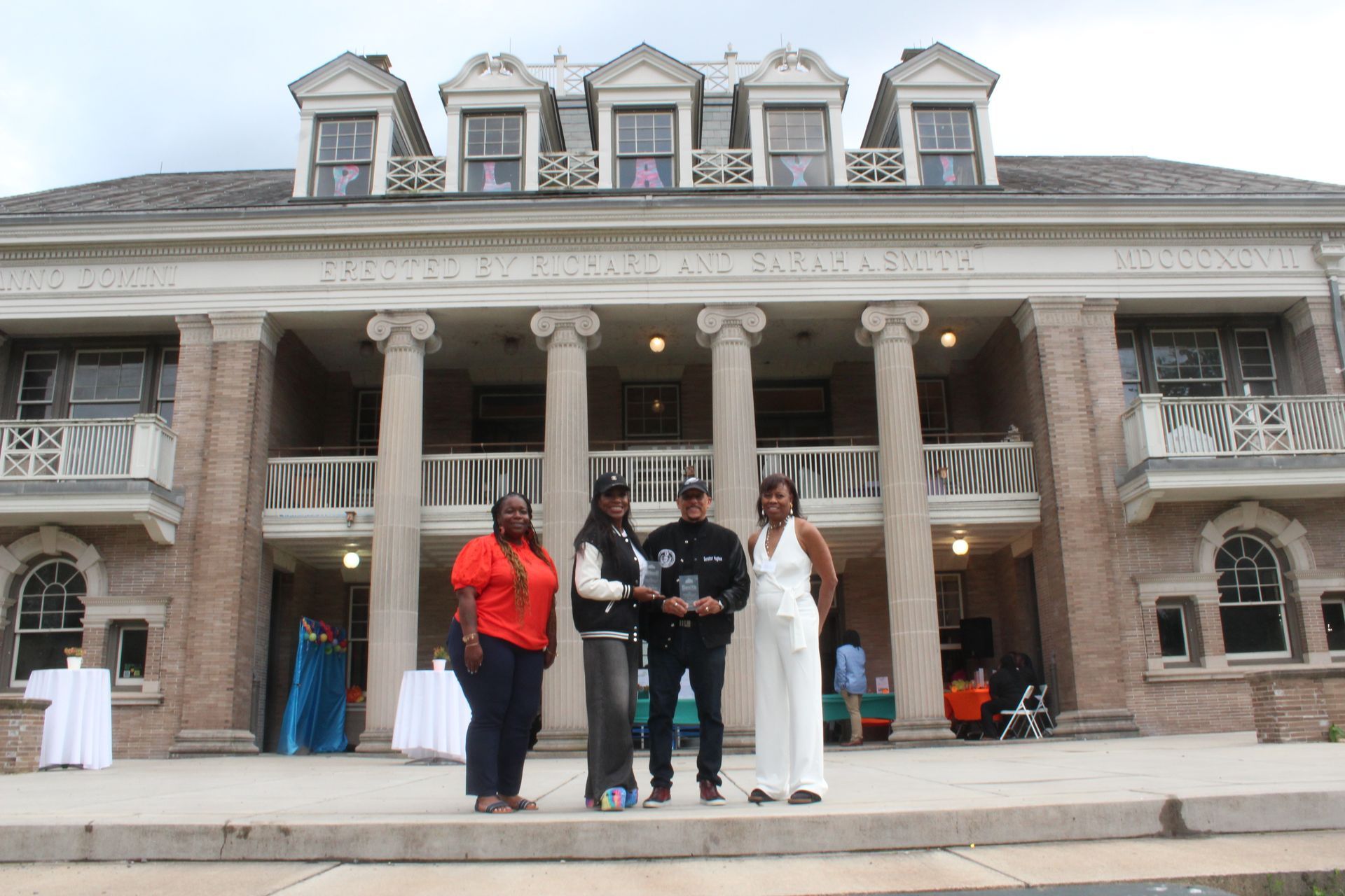 People posing on steps in front of a large historic mansion with columns and ornate windows