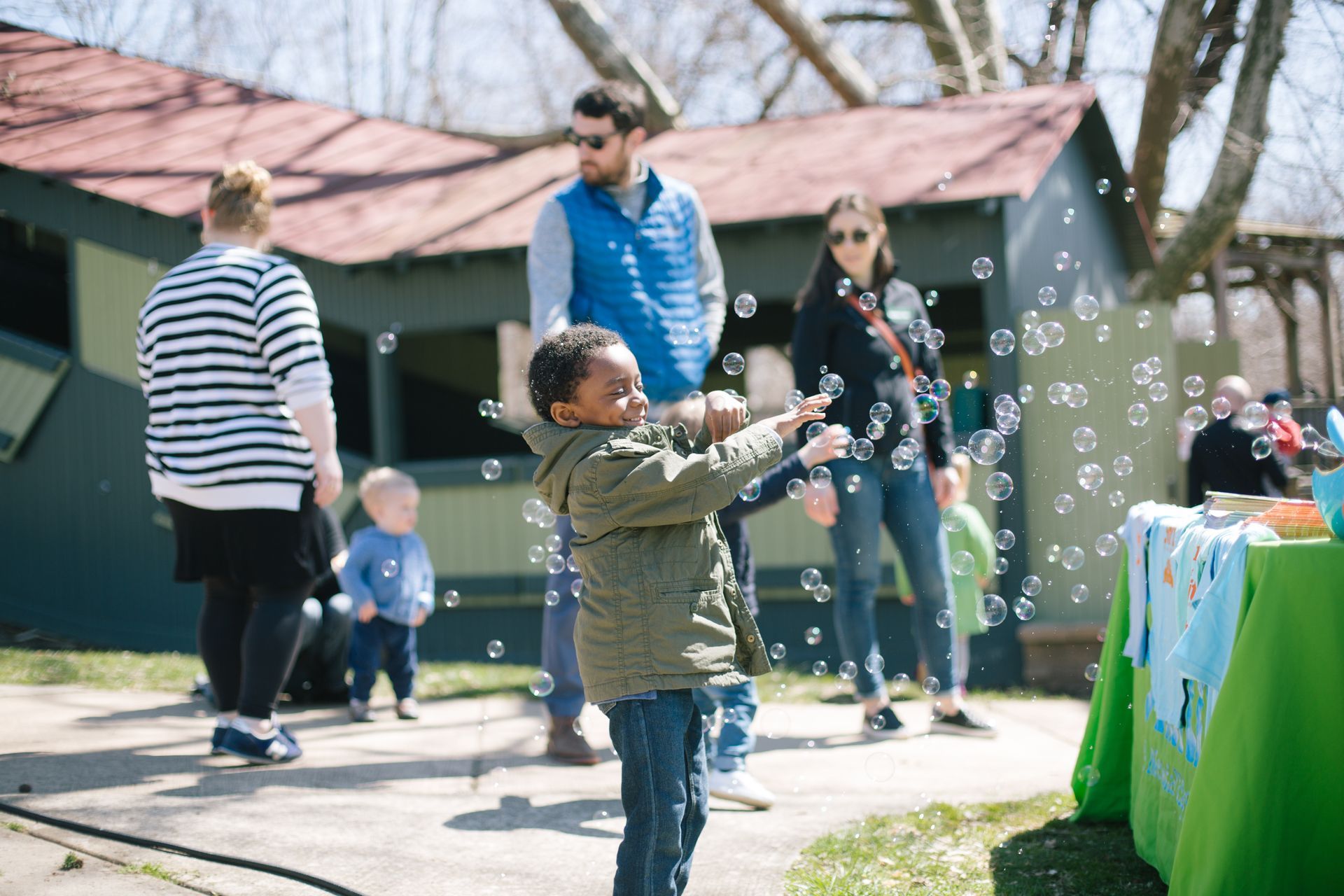 Child blowing bubbles outdoors at a park gathering with adults nearby