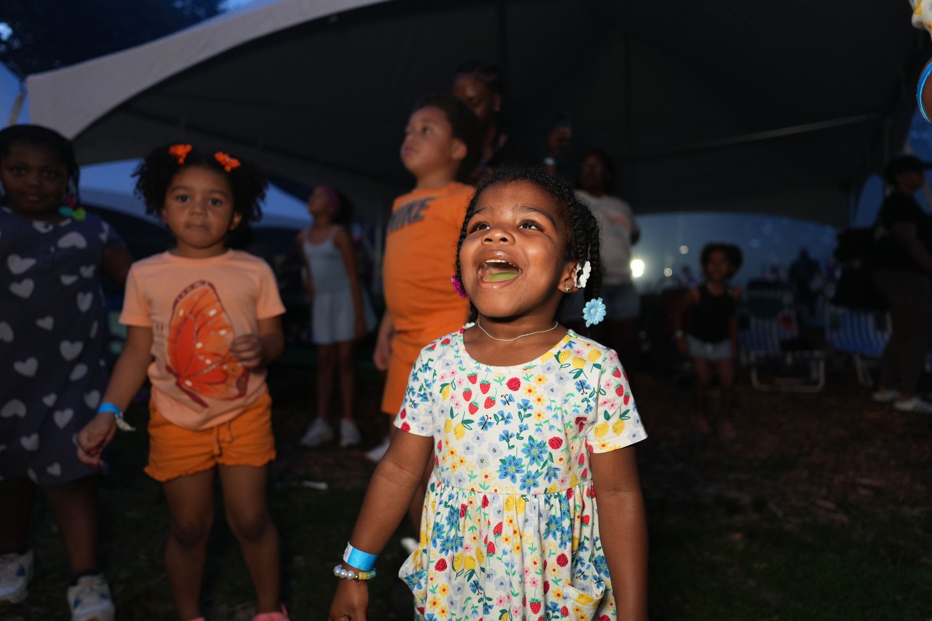 Children smiling and dancing under colorful lights at an outdoor nighttime event