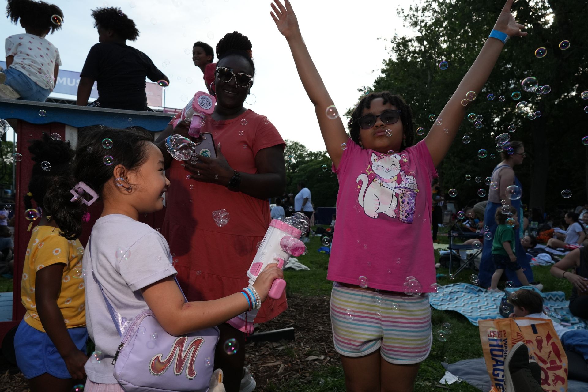 Children playing outdoors at a festival, one holding up colorful treats while another raises both arms in excitement