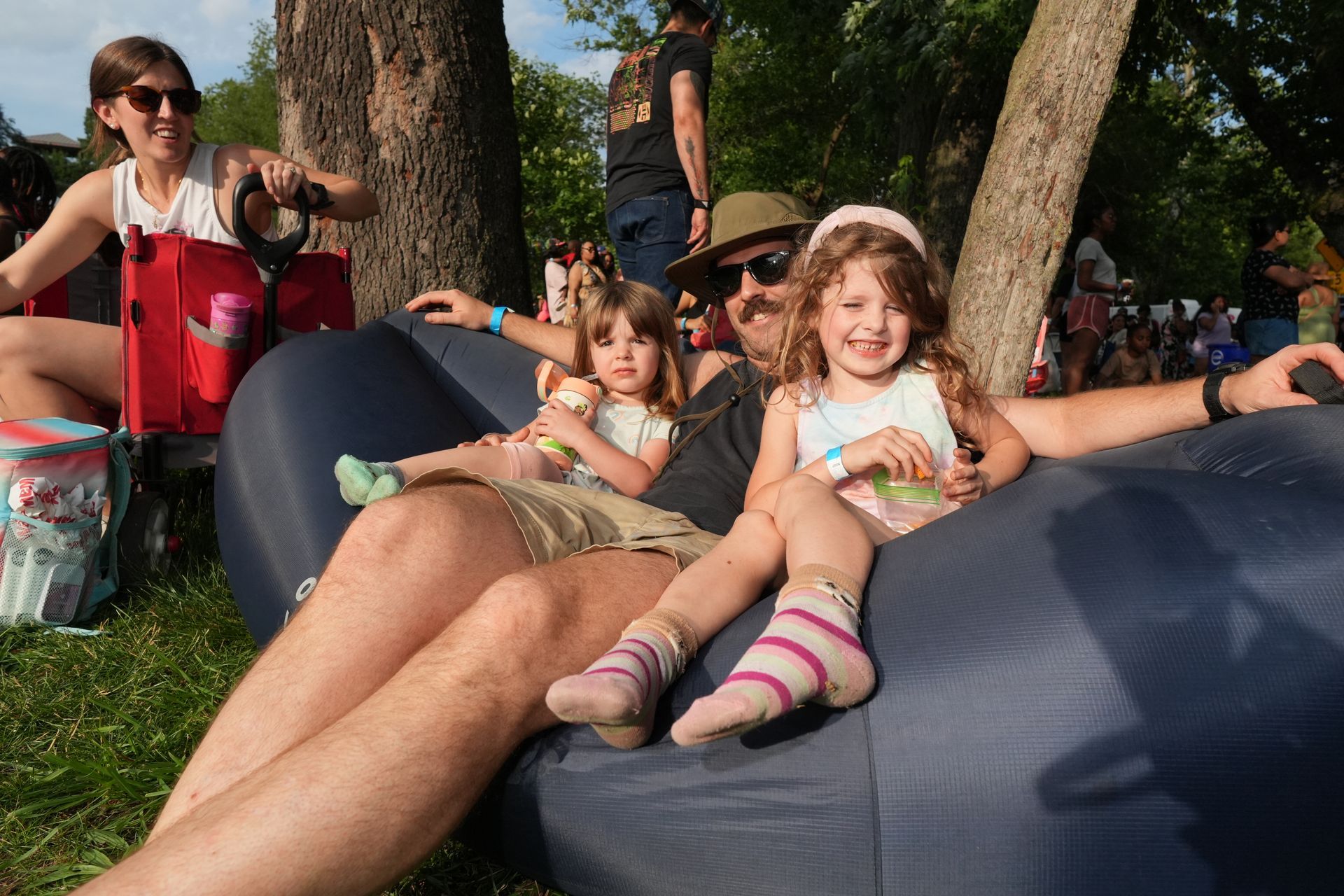 Children lounging on large blue beanbags outdoors near trees, smiling in a sunny park.