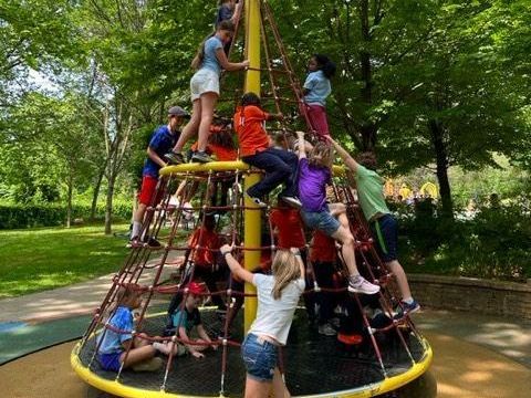 Children climbing on a colorful rope playground pyramid in a park