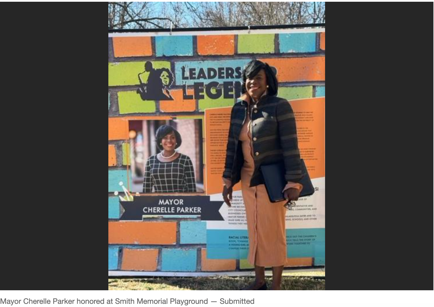Two people stand before a colorful “Leaders” mural, one holding a sign, outdoors.