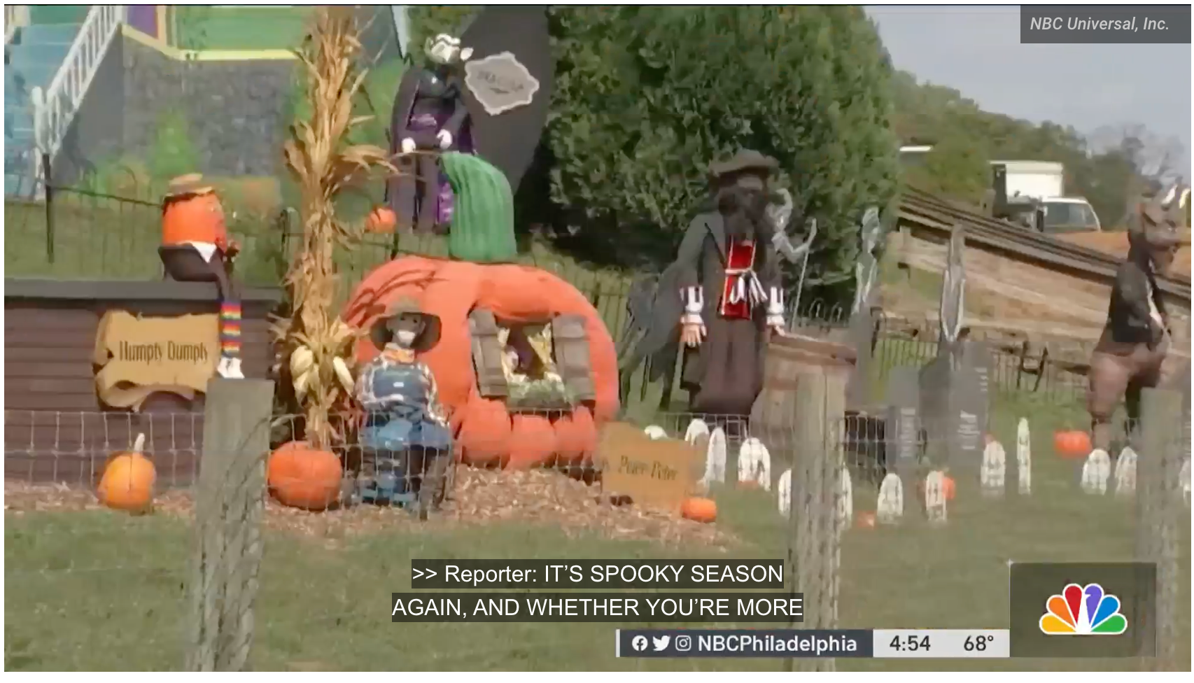 Pumpkin patch display with Halloween decorations, signs, and carved pumpkins by a roadside fence.