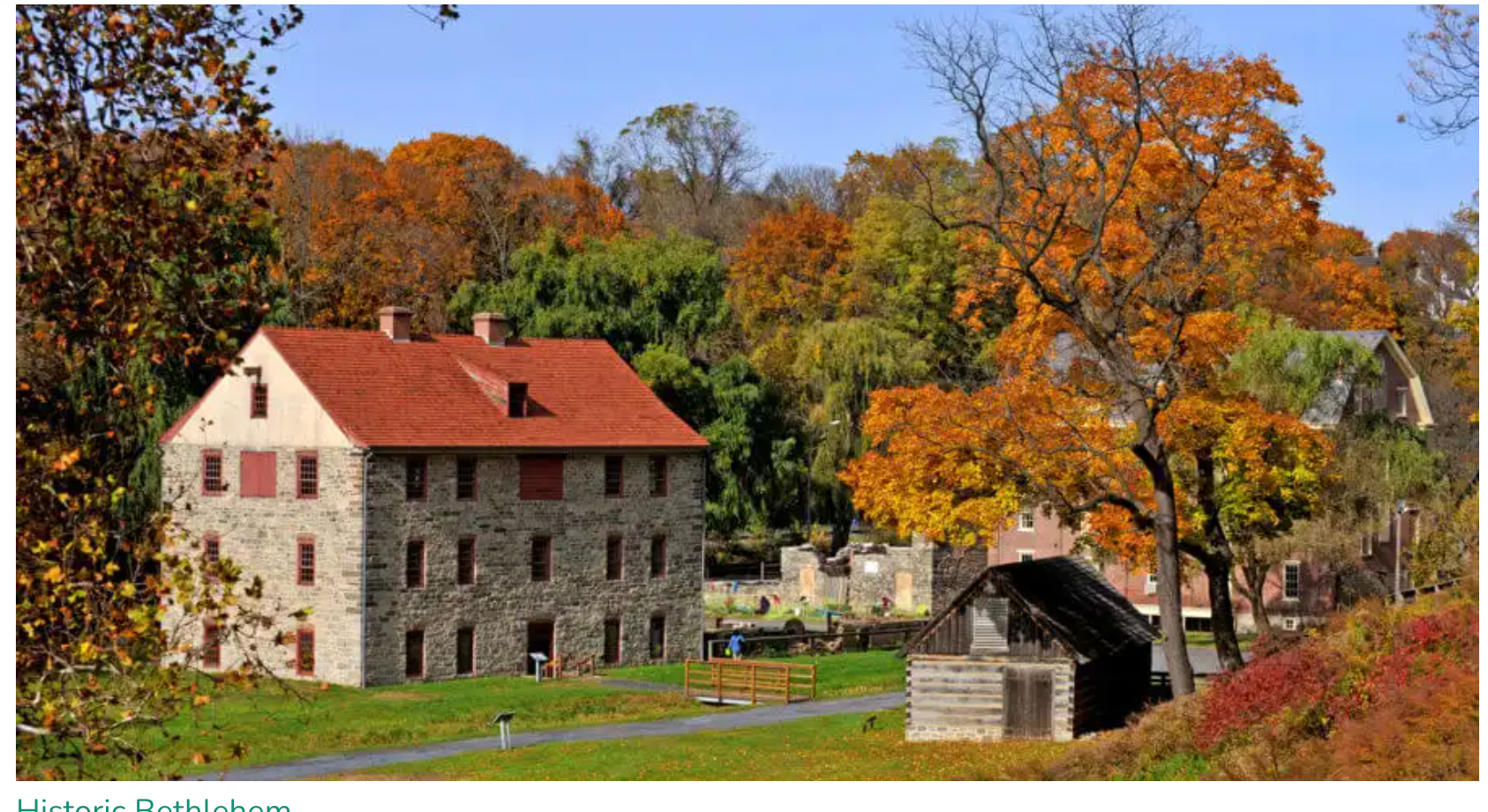 Autumn landscape with a historic stone mill, red roof, and colorful trees by a small stream