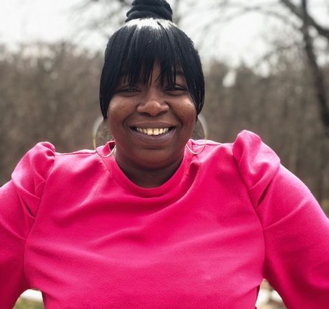 Smiling person in a bright pink top outdoors with bare trees in the background