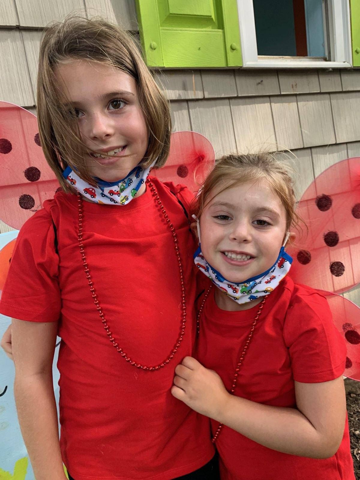 Two children in red shirts standing outdoors in front of a butterfly mural, smiling at the camera