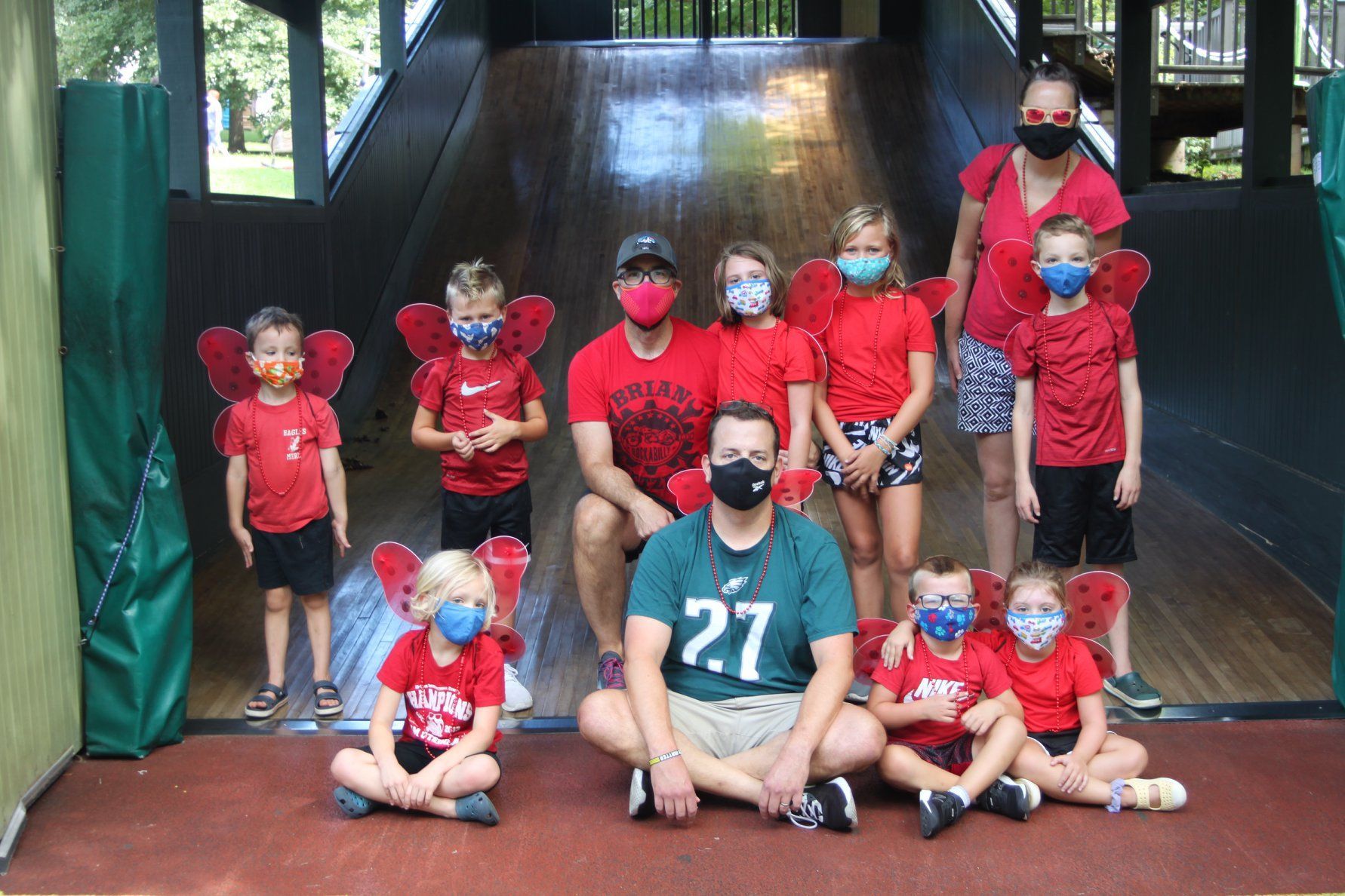 Group of children in red shirts and masks posing with two adults on a stage outdoors
