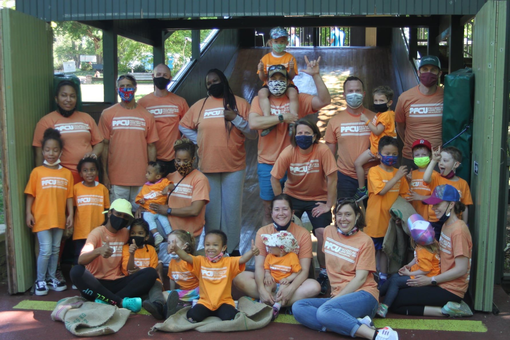 Group of people in orange shirts posing together outdoors in front of a wooden structure