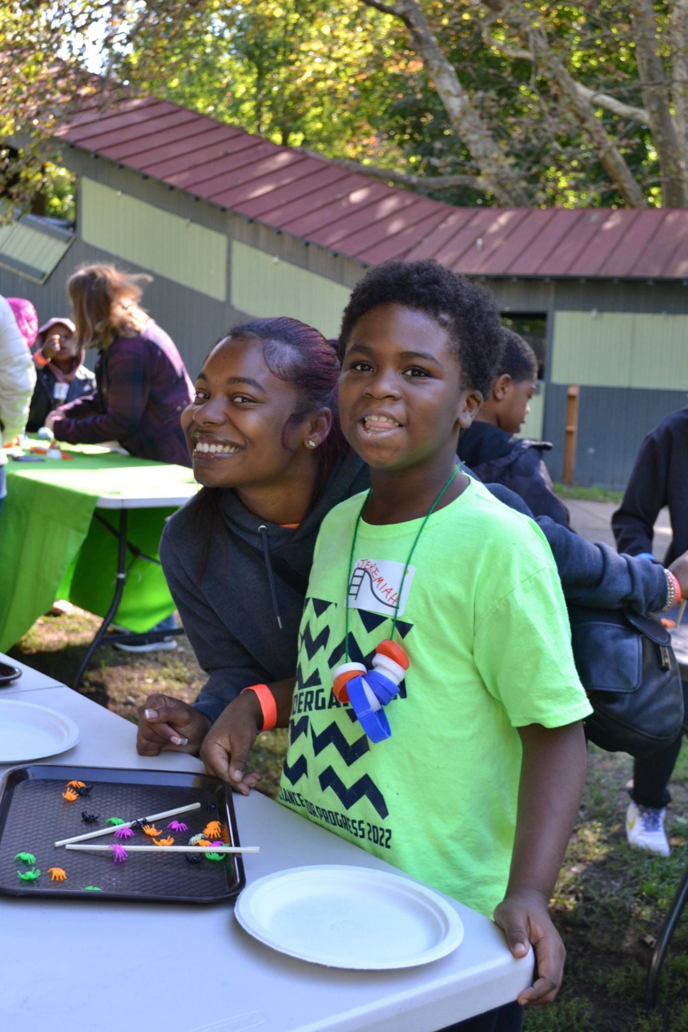 Two smiling children stand by a table with candy and plates at an outdoor event.