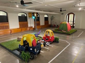 Indoor play area with toy cars, a small tent, and a train crossing sign on a gray floor.