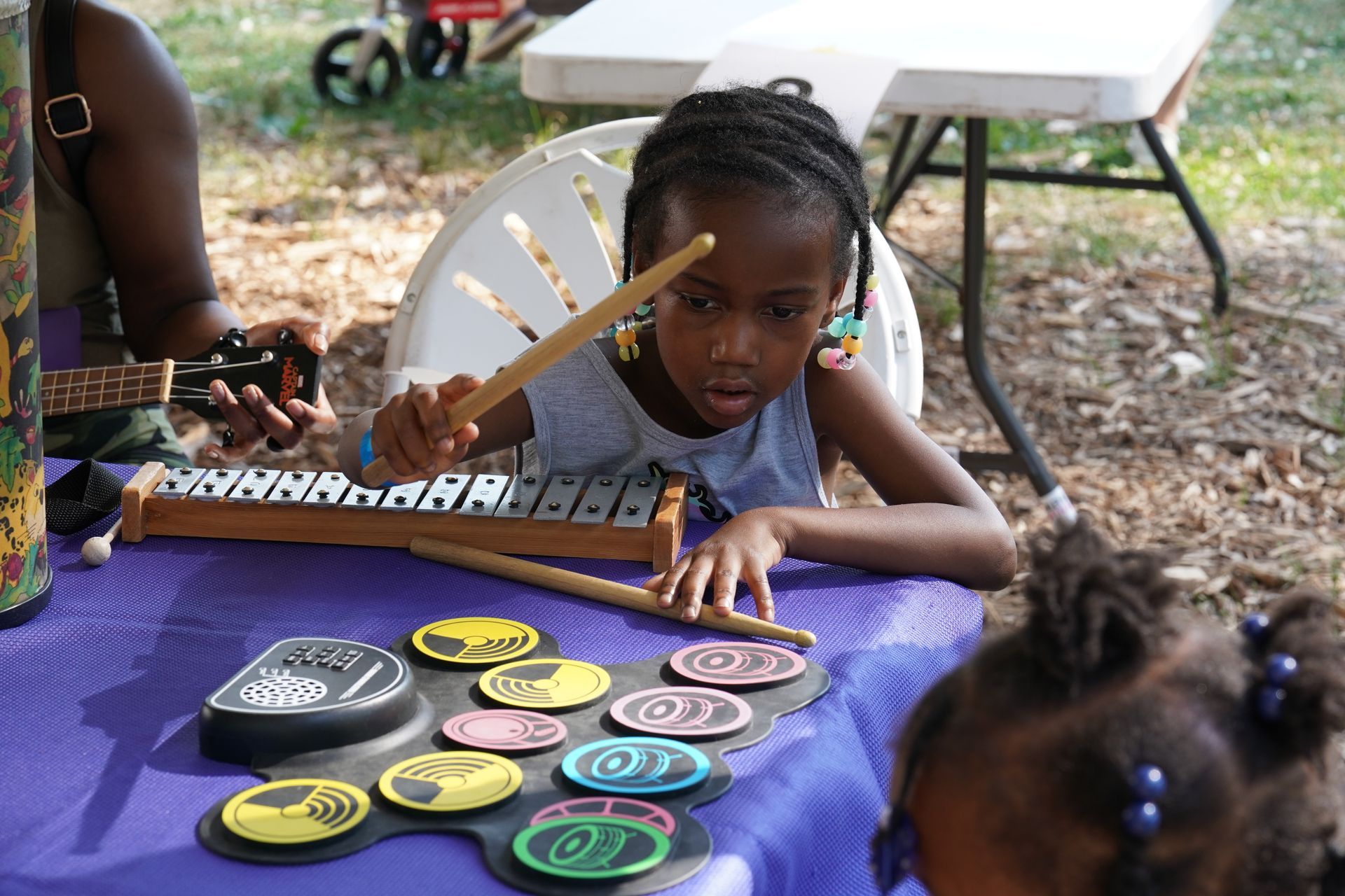 Girl leaning on a purple table with colorful game pieces and a wooden board outdoors