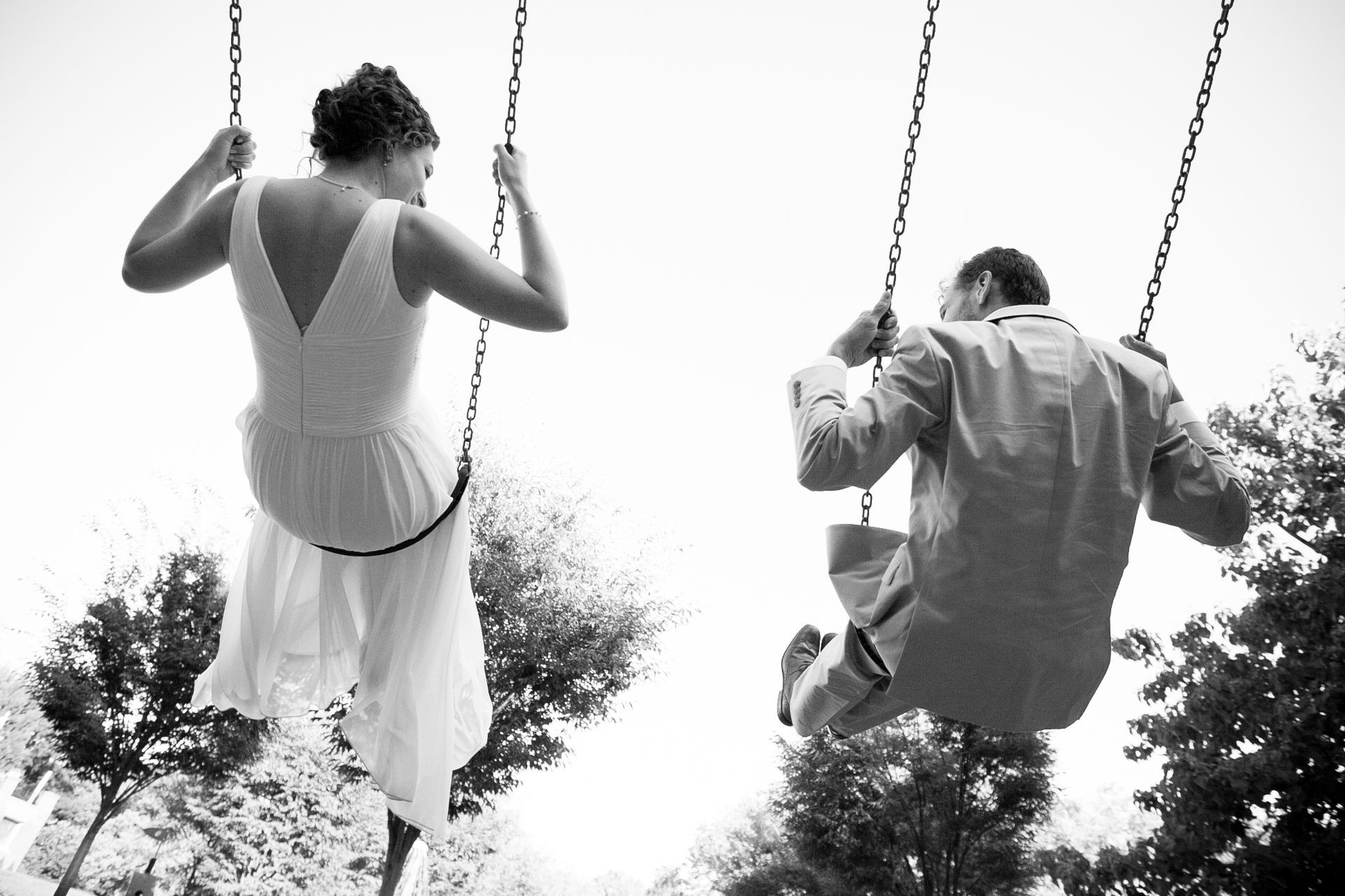 Two people on swings, seen from behind, in a black-and-white outdoor scene