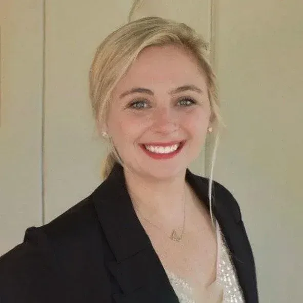 Blonde woman in black blazer smiles, looking at the camera.