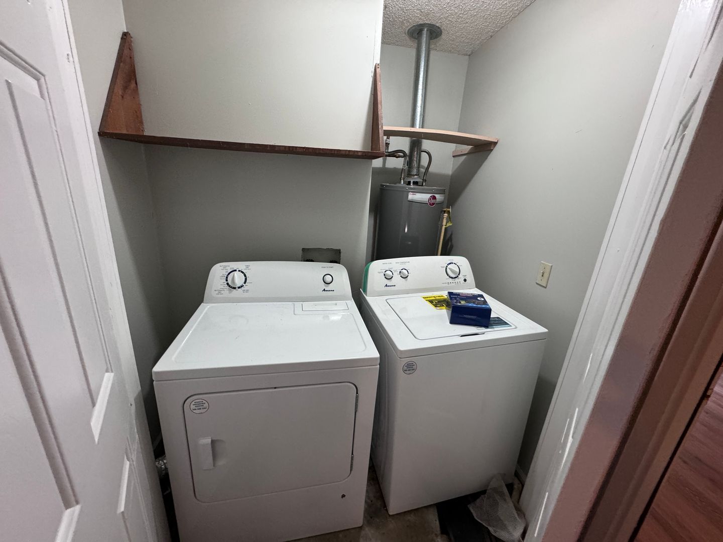 Laundry room with a white dryer and washing machine, shelving, and a water heater.