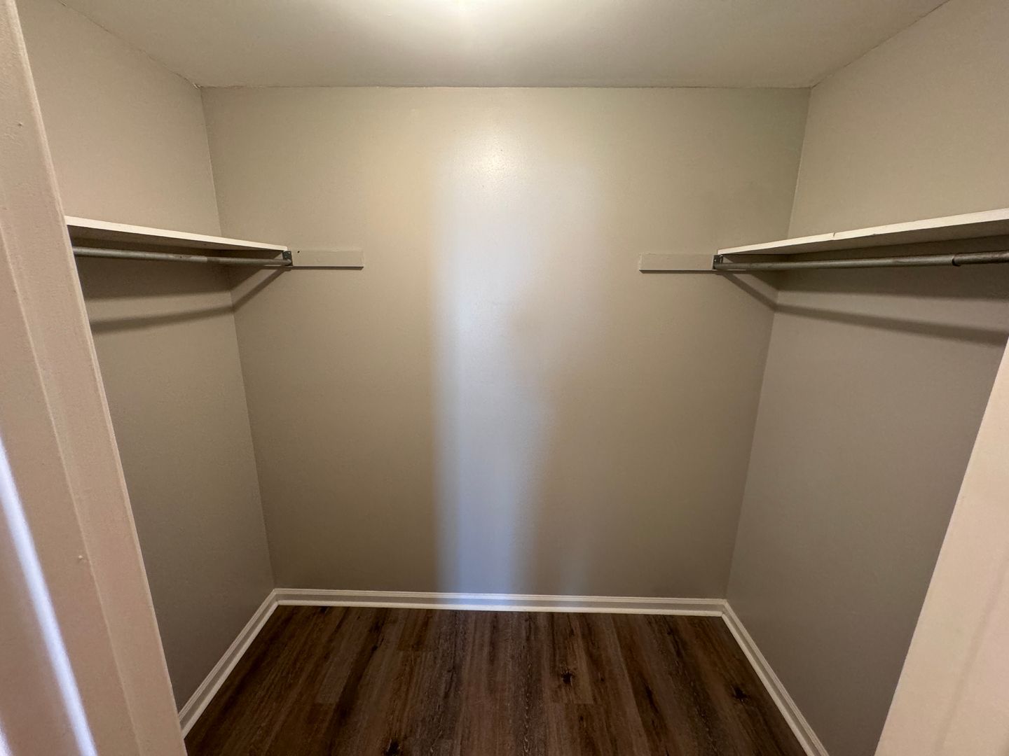 Empty walk-in closet with shelves and a dark wood floor. Beige walls and white trim.