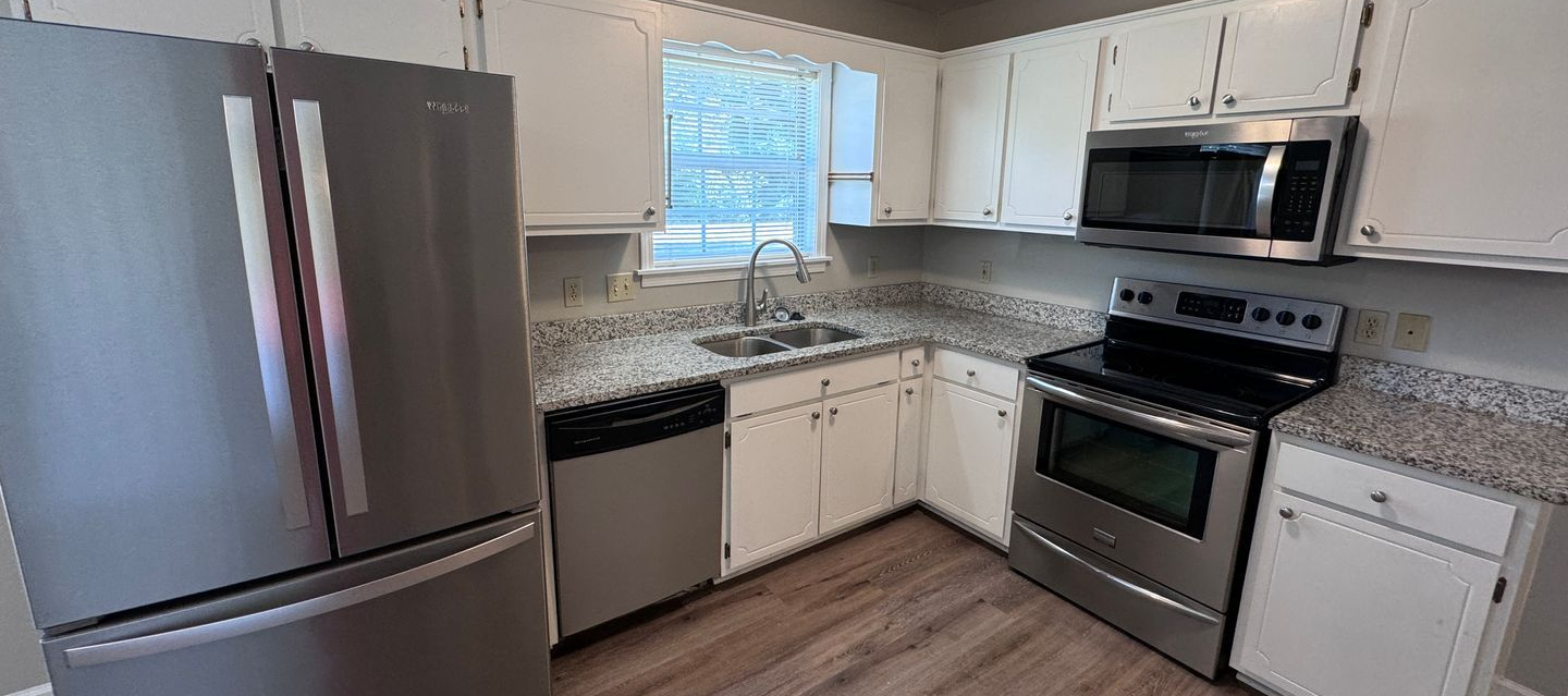 Kitchen with stainless steel appliances, white cabinets, and speckled countertops.