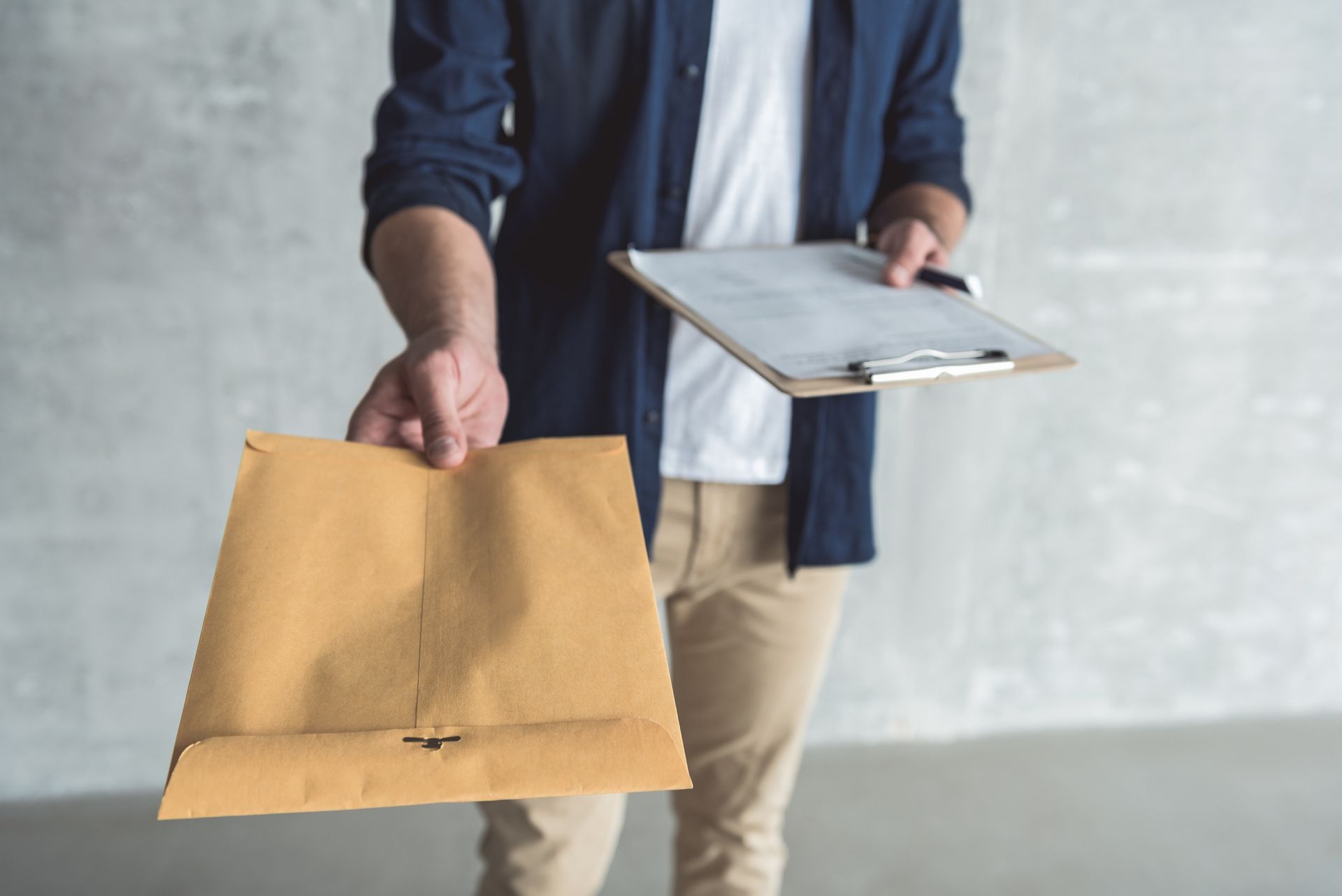 Person holding out a large brown envelope and clipboard.
