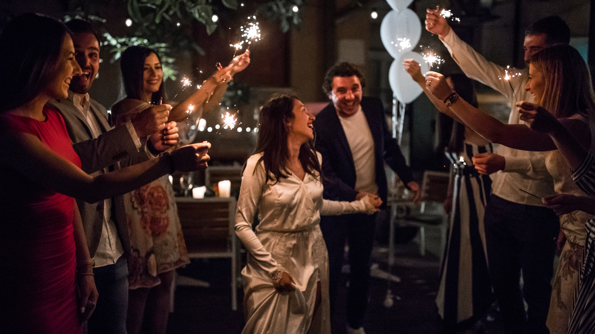 A group of people are holding sparklers at a wedding reception.