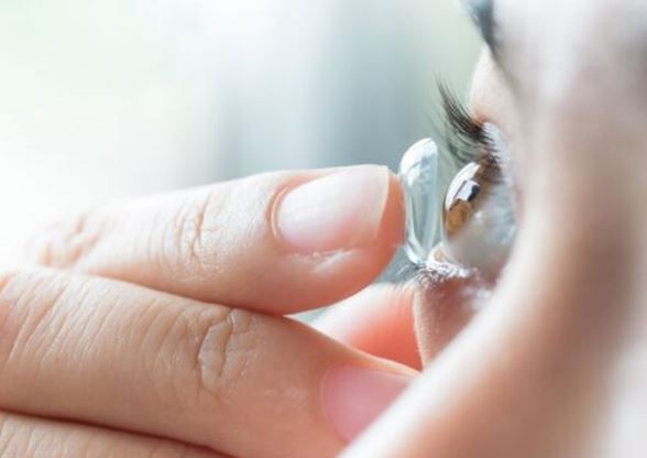 Person inserting a contact lens into their eye. Close-up of the hand holding and placing the lens.