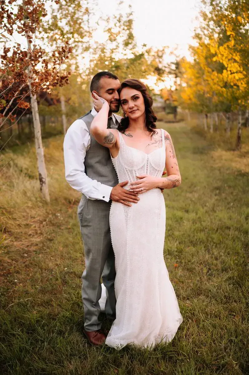 Couple embracing in a grassy field at sunset, with golden autumn trees in the background.