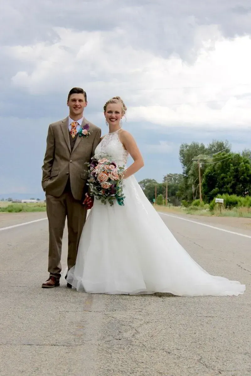 Bride and groom standing on a rural road, the bride in a white gown holding a bouquet.