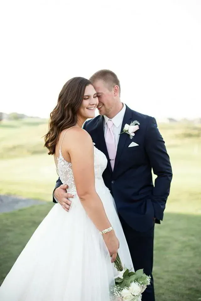 Bride and groom embracing outdoors, smiling in formal wedding attire.