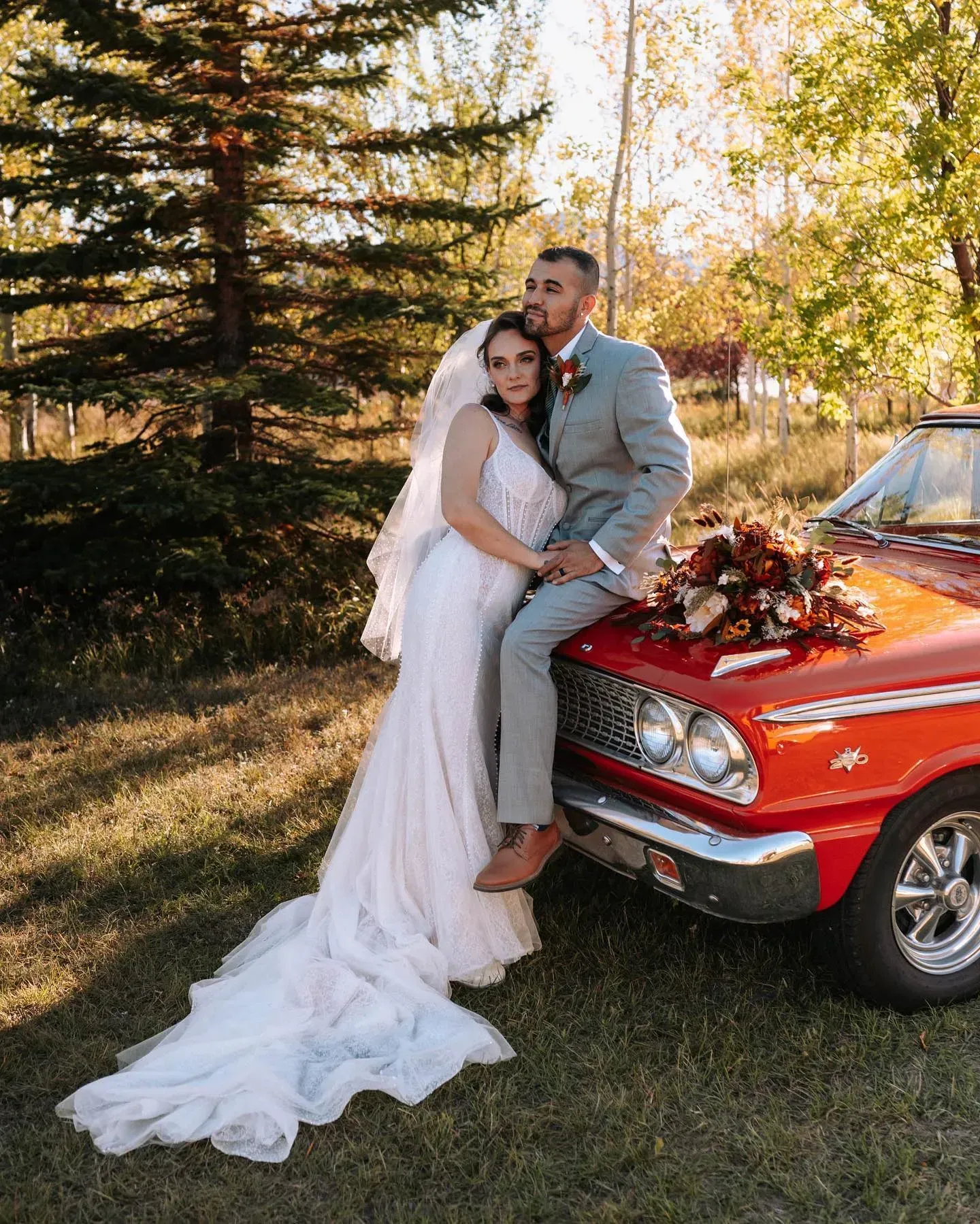 Bride and groom posing beside a red vintage truck outdoors in autumn.