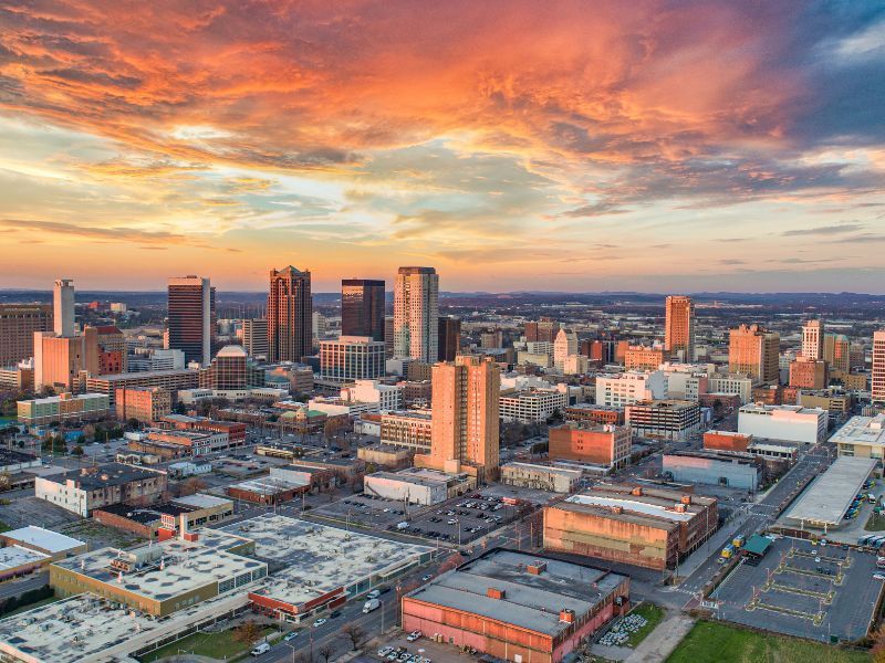 Aerial view of a city skyline at sunset with glowing orange clouds and downtown buildings.