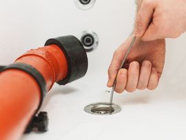 Hand pulling a drain chain beside a red pipe under a sink
