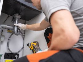 Plumber repairing pipes under a sink with a power drill in a kitchen cabinet