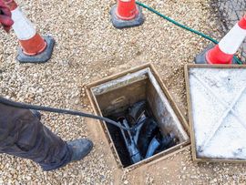 Worker inspecting an open utility manhole with a cable, surrounded by traffic cones