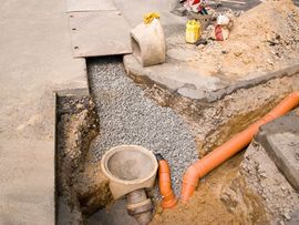 Damaged concrete trench with exposed drainage pipe and gravel beside a roadside curb
