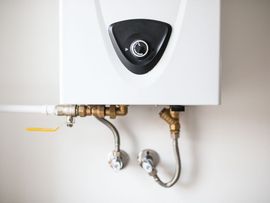 Wall-mounted white water heater with exposed pipes and valves against a light wall.