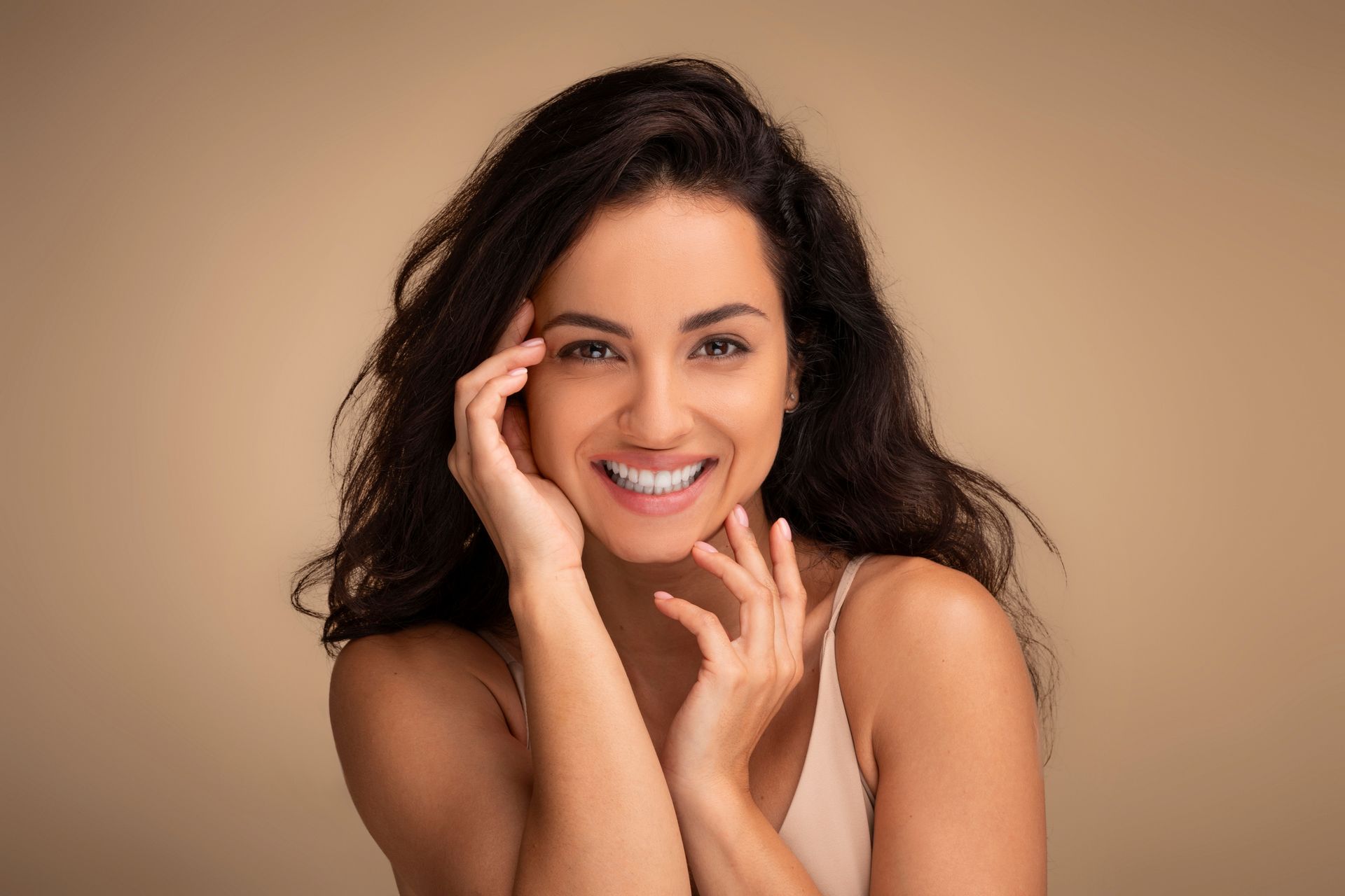 Woman smiles with hands near face.