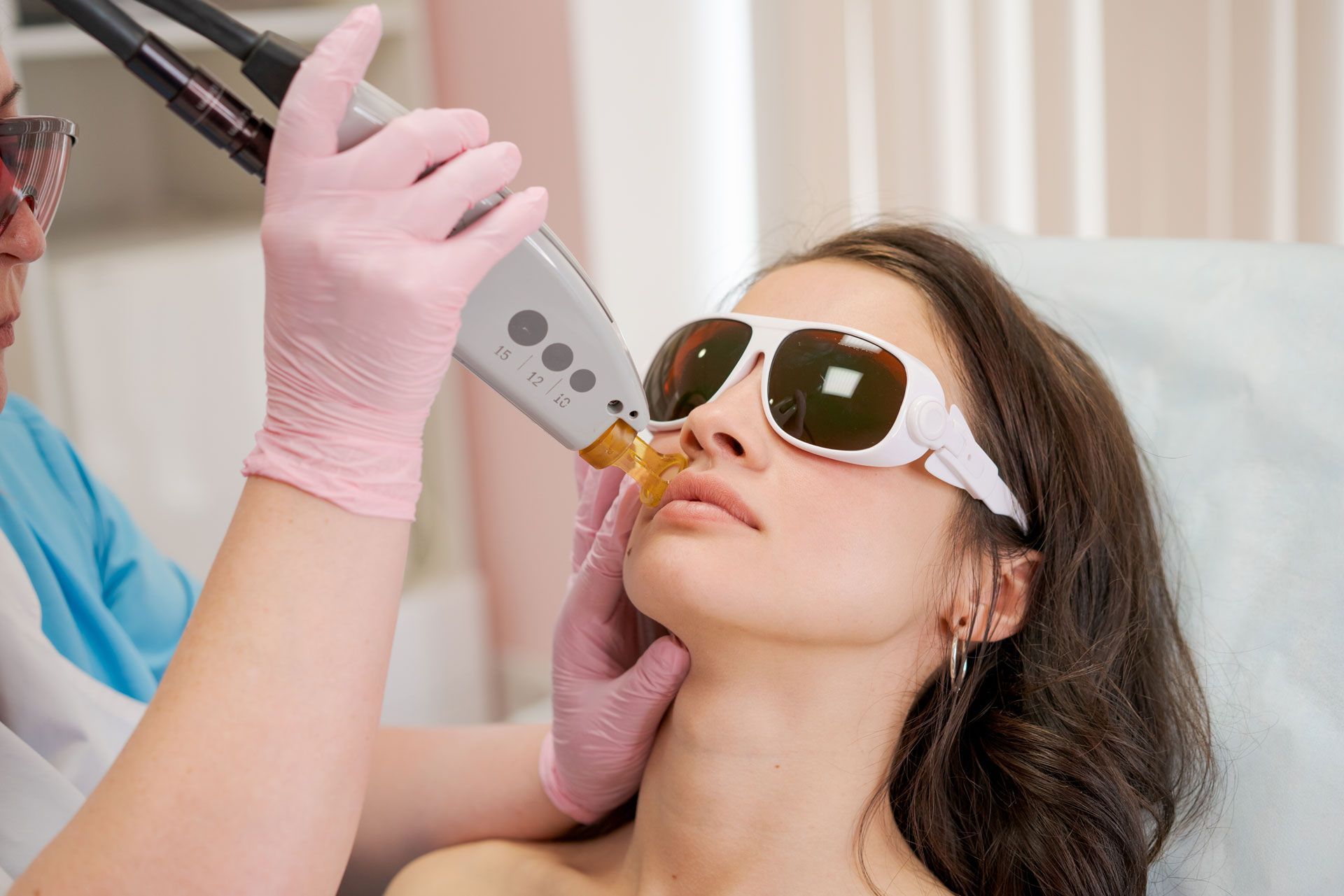 A gloved clinician uses a laser device near a patient wearing protective goggles.