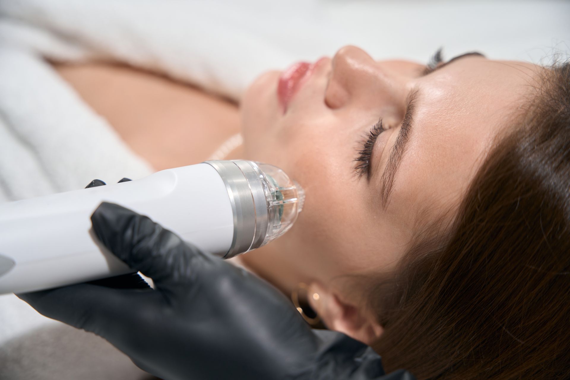 Woman receiving a facial treatment with a handheld device and gloved technician