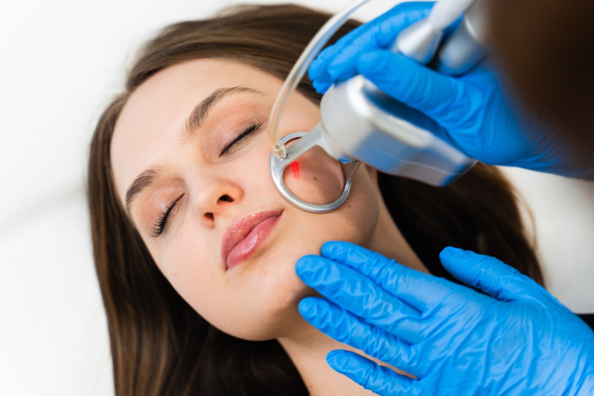Person receiving a facial treatment with a metal tool while lying with eyes closed