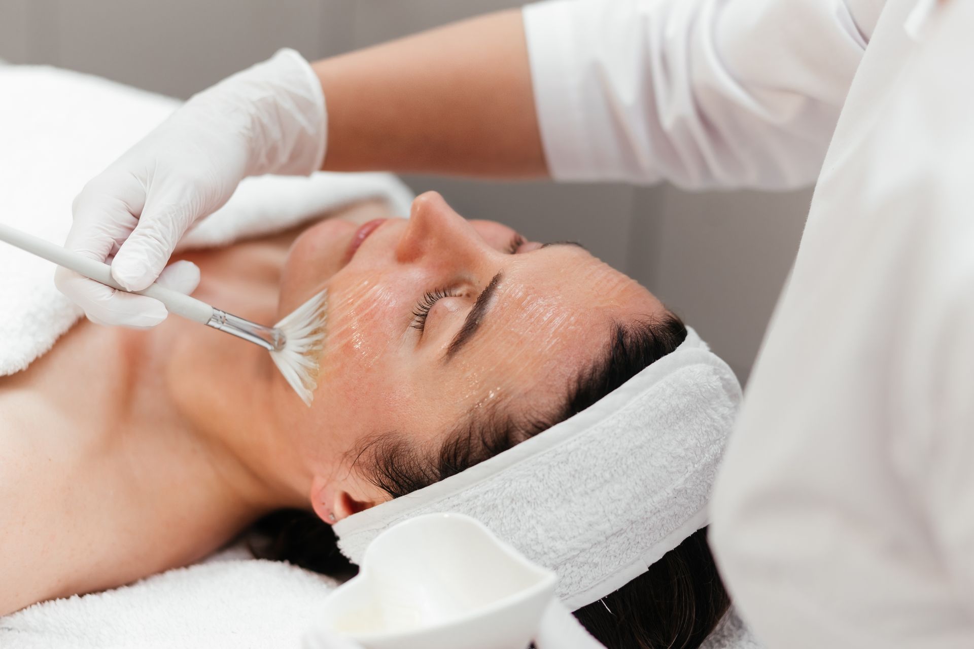 Facial spa treatment with a gloved esthetician applying a mask to a reclining client