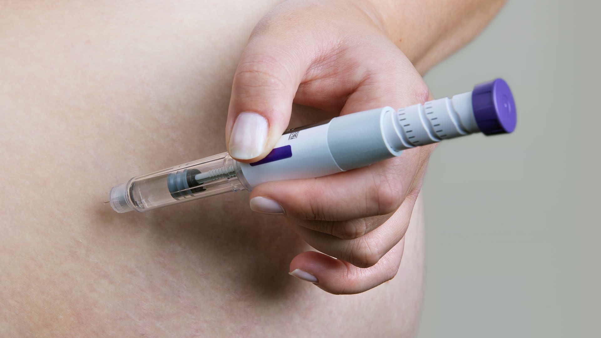 Close-up of a hand injecting medicine with an insulin pen into the abdomen