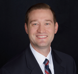 Portrait of a smiling man in a dark suit, white shirt, and striped tie against a black background