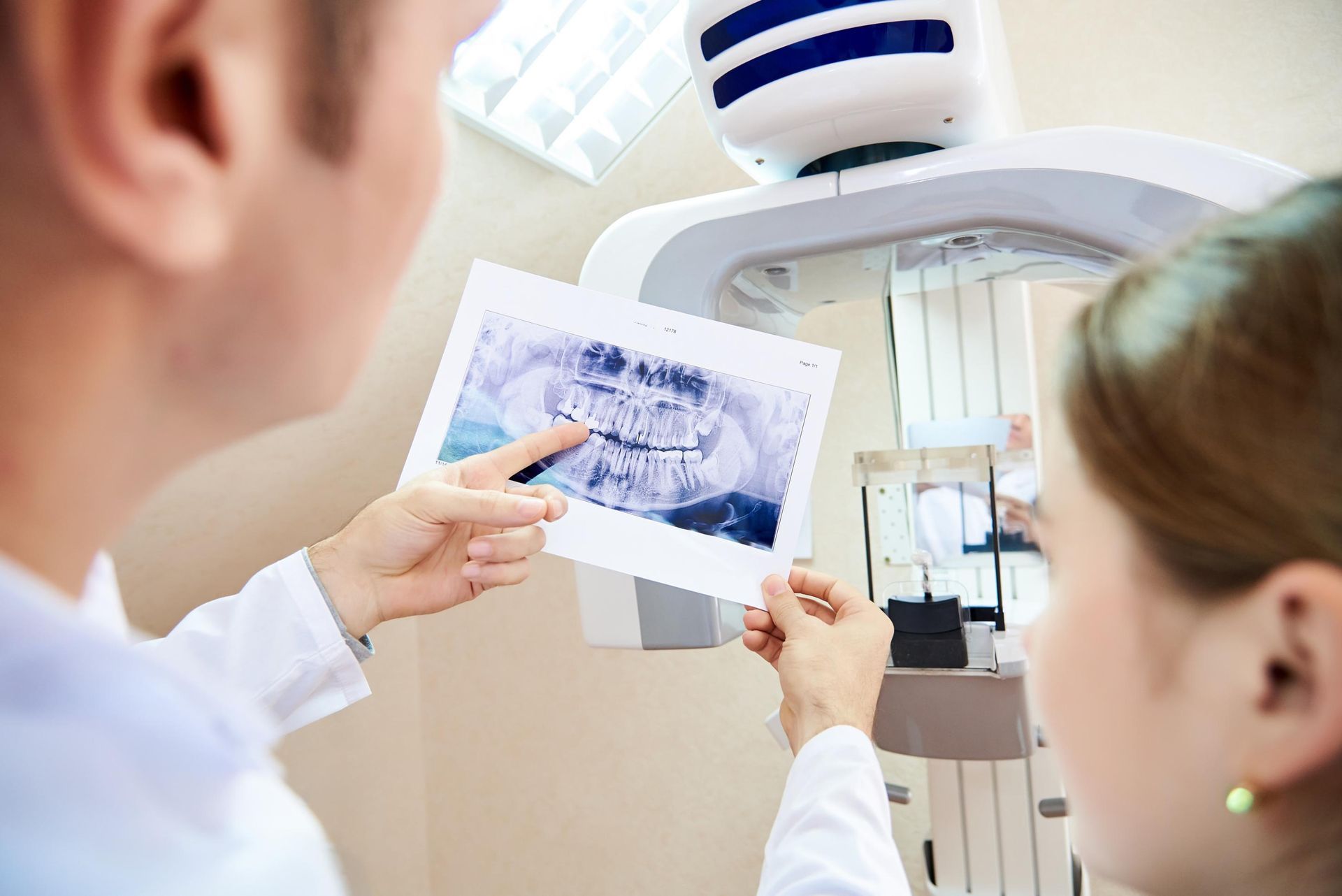 Two people examining dental X-rays beside a panoramic dental machine.