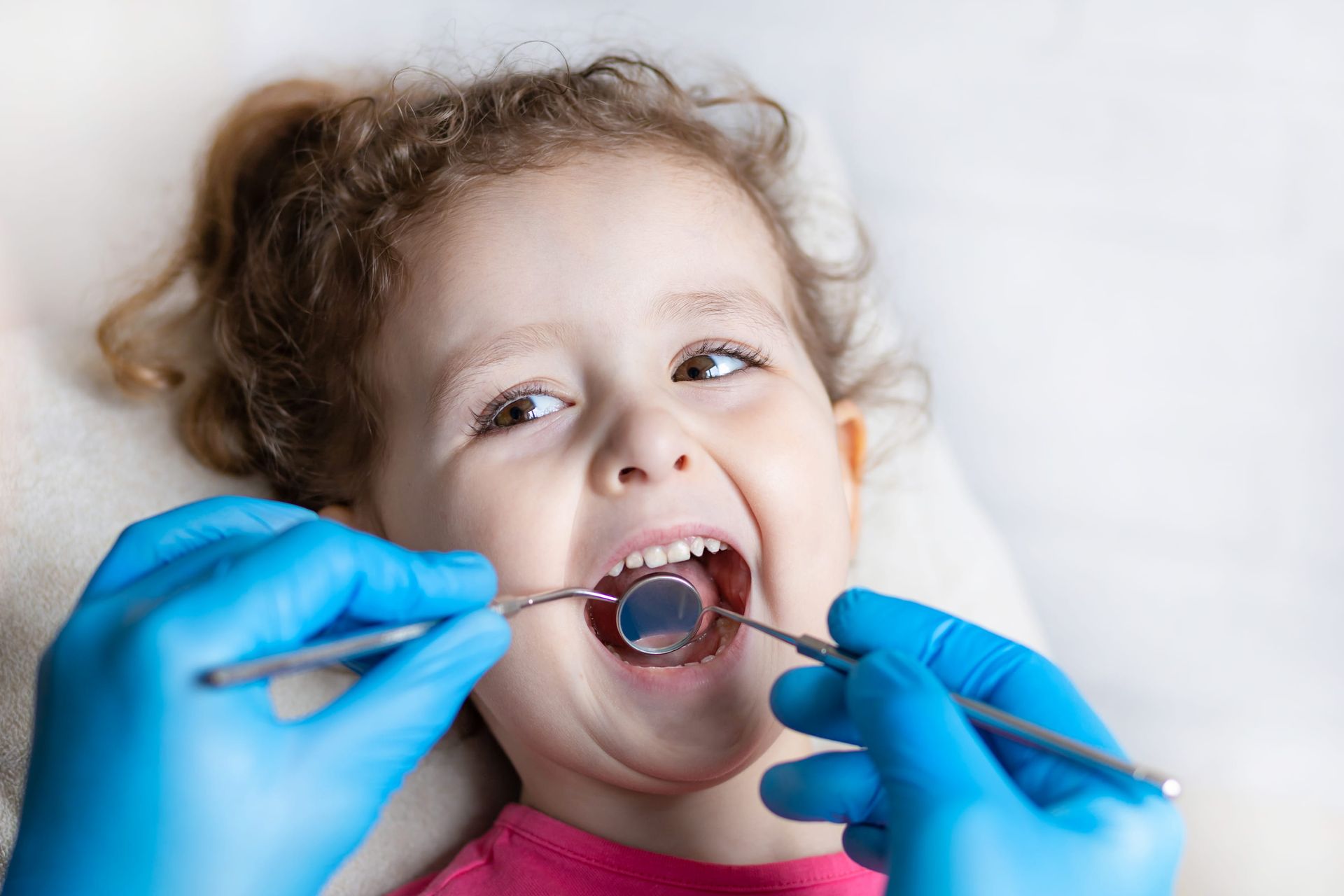 Child at dentist with open mouth while gloved hands use dental tools